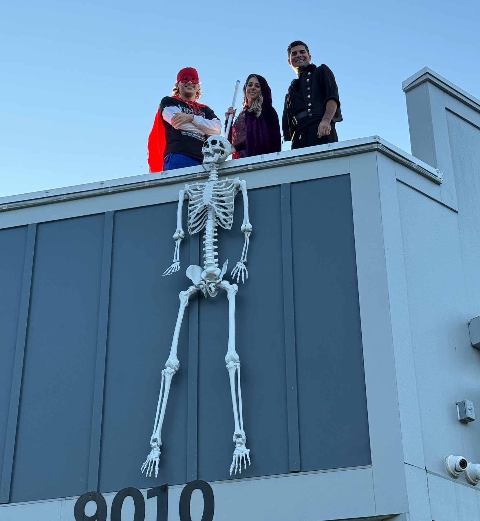 Costumed team members posing on the office roof beside a skeleton